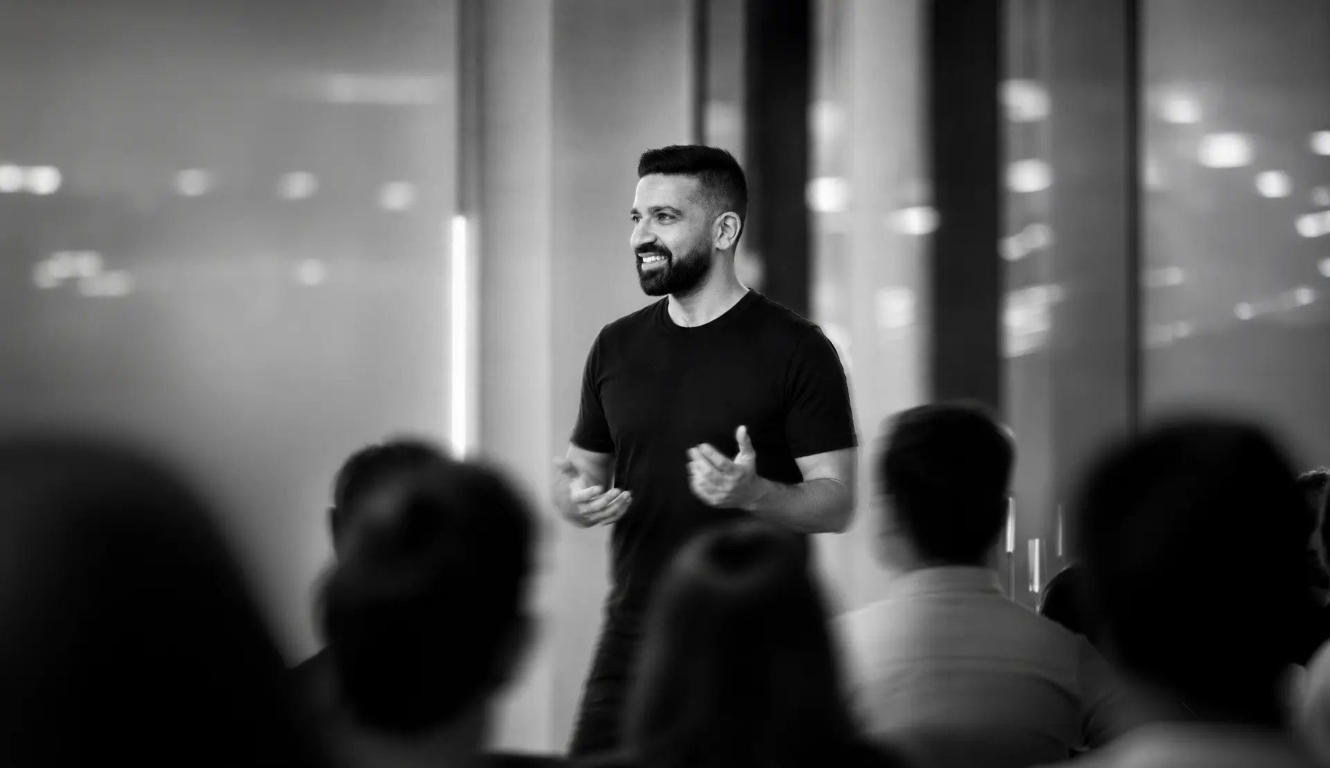 Faheem Chaudhry speaking on stage to an audience, in black and white